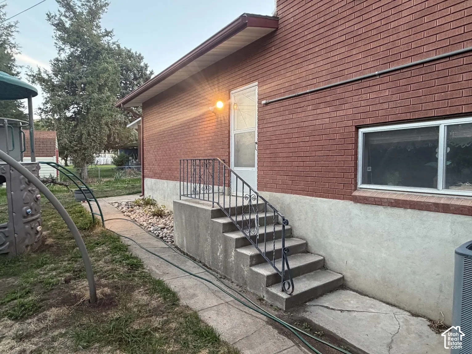 Brick exterior with a concrete foundation, featuring a rear entry door with a storm door, and a concrete staircase with metal railings