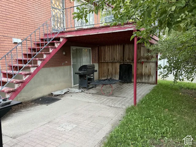 Brick exterior with exterior staircase featuring wrought iron railing, concrete patio, and covered outdoor area