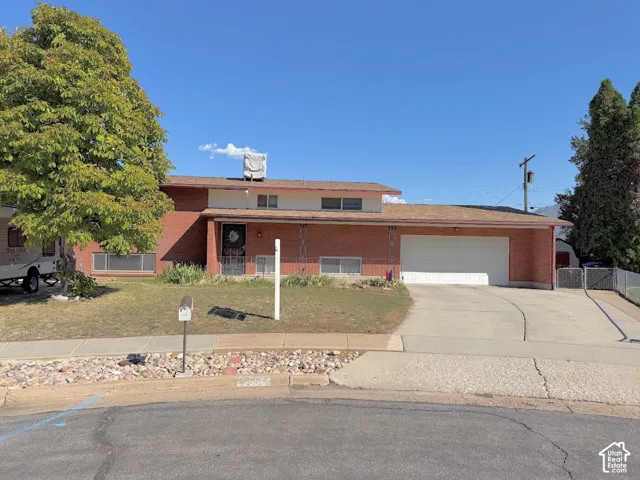Brick exterior with a two-car garage, mature trees, and a paved driveway