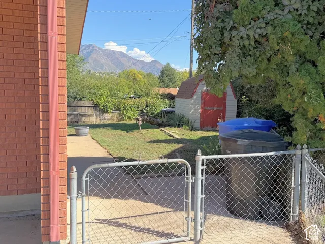 Expansive backyard featuring a chain link fence, concrete patio, grass lawn, and a storage shed
