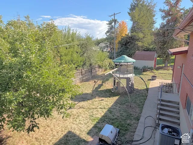 Expansive backyard featuring a privacy fence, mature trees, concrete patio, and exterior brick siding