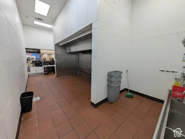 Commercial kitchen area featuring tile flooring, white panel walls, and stainless steel fixtures