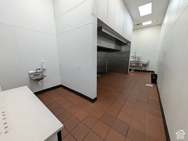 Commercial kitchen space featuring tile flooring, stainless steel sink, wall-mounted hand sink, and an exhaust hood