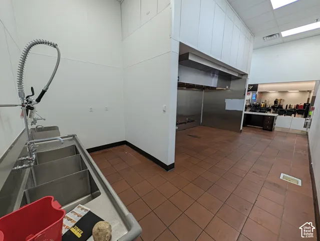 Industrial-grade three-compartment stainless steel sink with pre-rinse sprayer, stainless steel wall paneling, and a commercial ventilation hood system