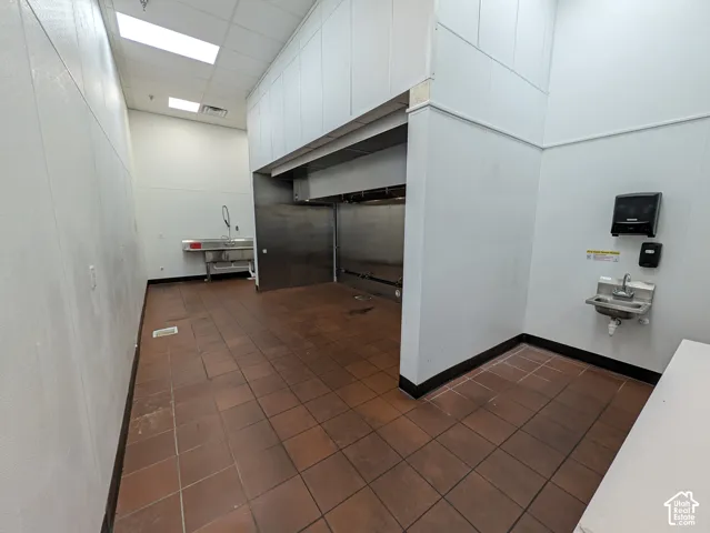 Commercial kitchen space featuring brown tiled flooring, stainless steel fixtures, a wash sink, and a handwashing station
