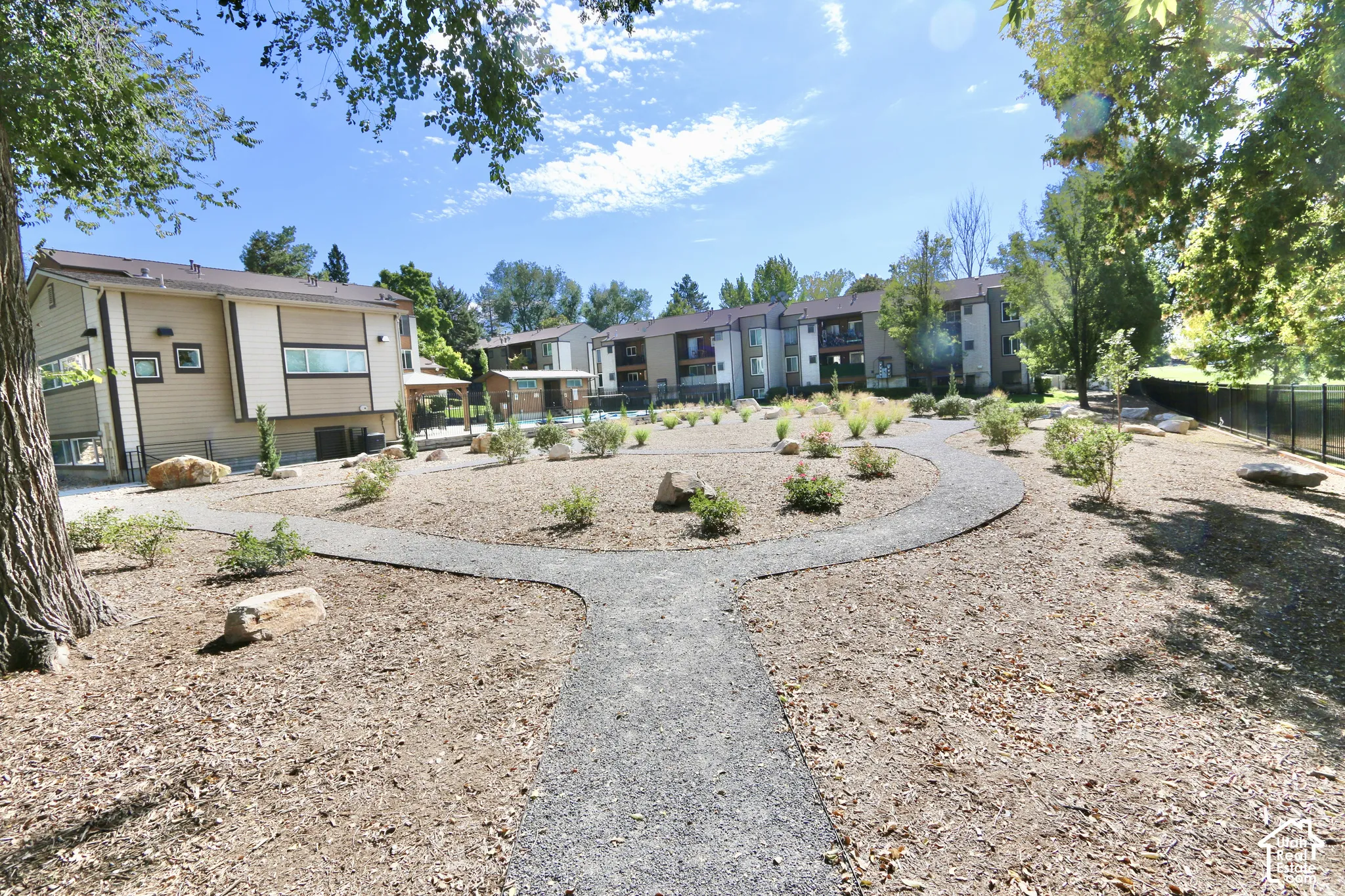 Expansive outdoor space featuring a winding gravel pathway, decorative landscaping with shrubs, and mature trees