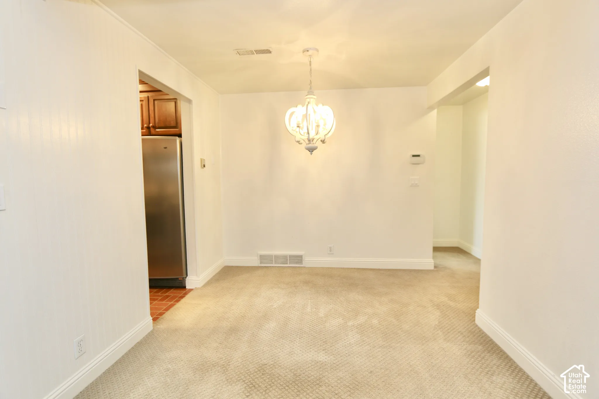 Carpeted room with a central chandelier, leading to an arched doorway