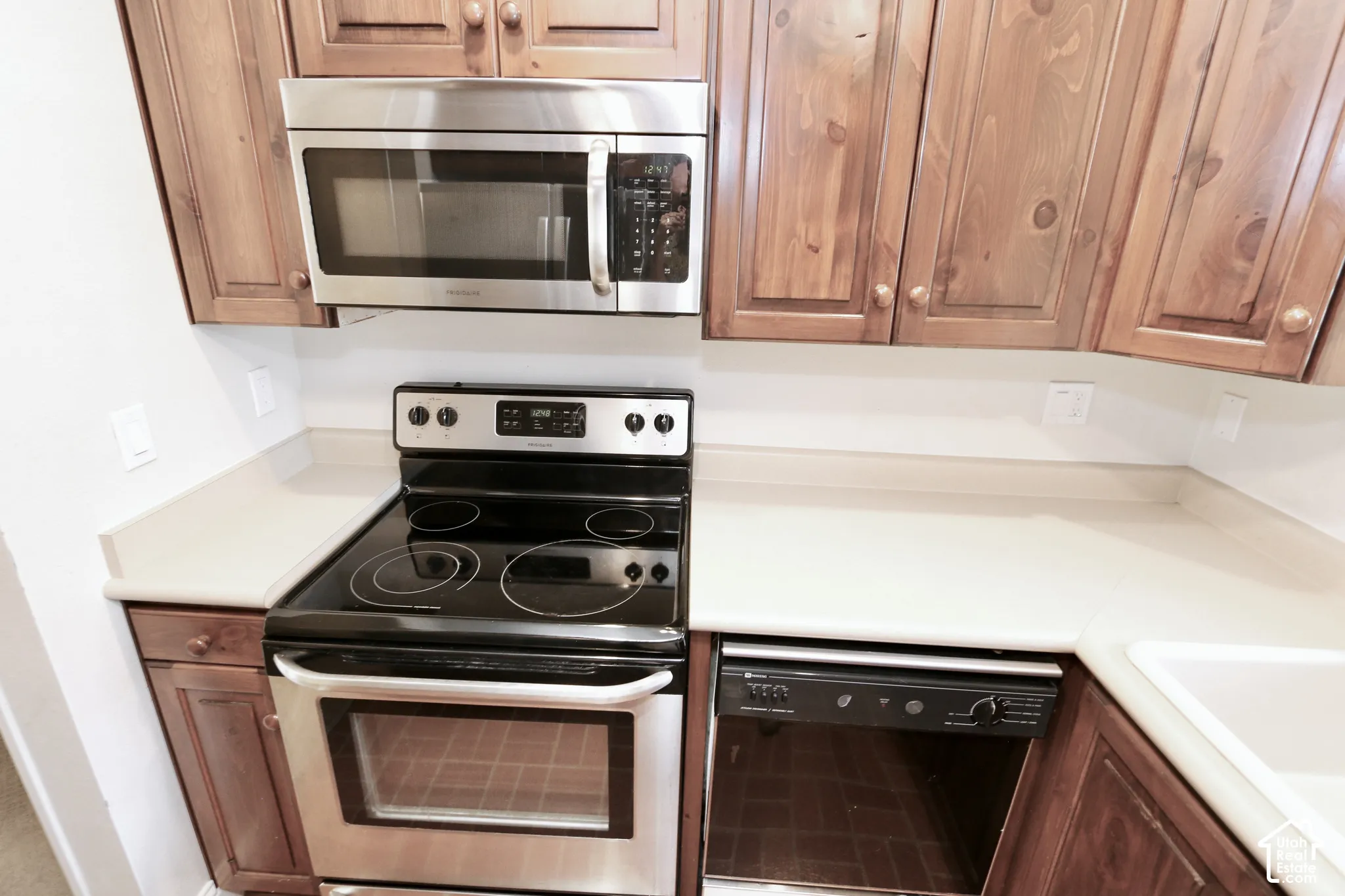 Stainless steel microwave, electric range, and integrated dishwasher complement light countertops and wood cabinetry