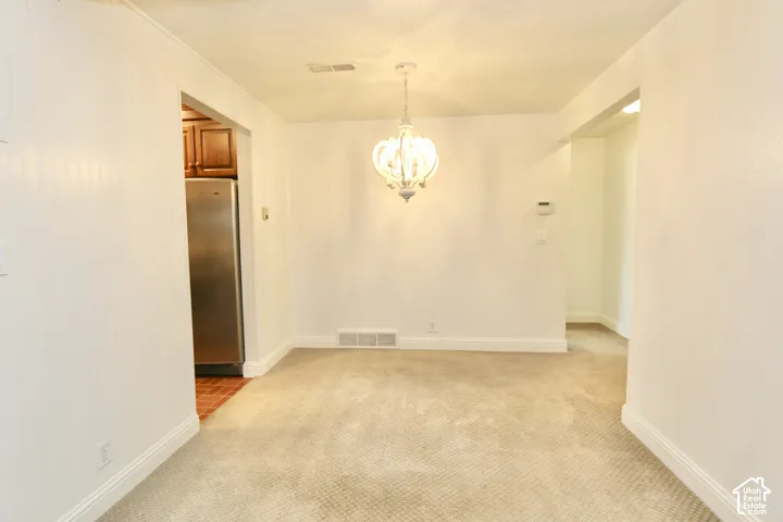 Carpeted room with a central chandelier, leading to an arched doorway