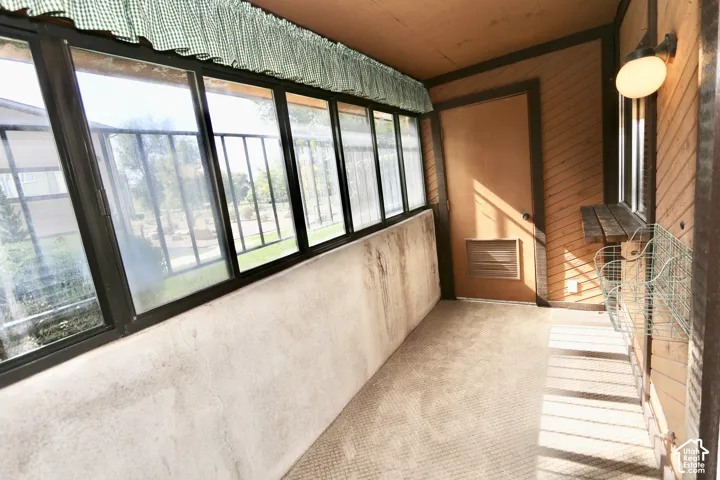 Enclosed sunroom featuring multiple large windows, wood-paneled walls, and a built-in wall light fixture