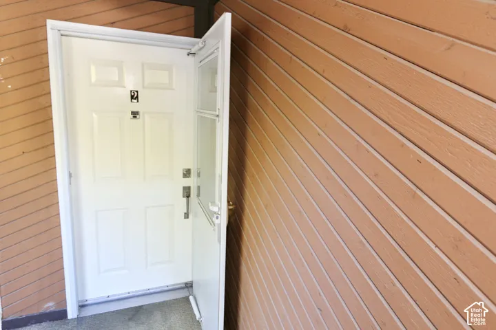 White paneled entry door with storm door, accompanied by horizontal wood-finish siding