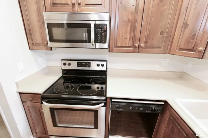 Stainless steel microwave, electric range, and integrated dishwasher complement light countertops and wood cabinetry