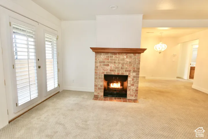 Brick fireplace with a wood-finish mantel, double French doors with plantation shutters, and light-toned carpeting