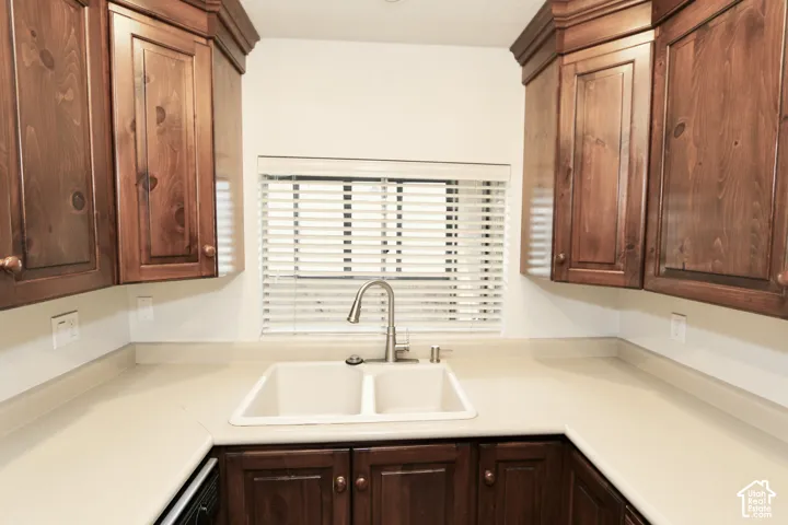 Wood cabinetry with crown molding, double basin sink, gooseneck faucet, and light-toned countertops