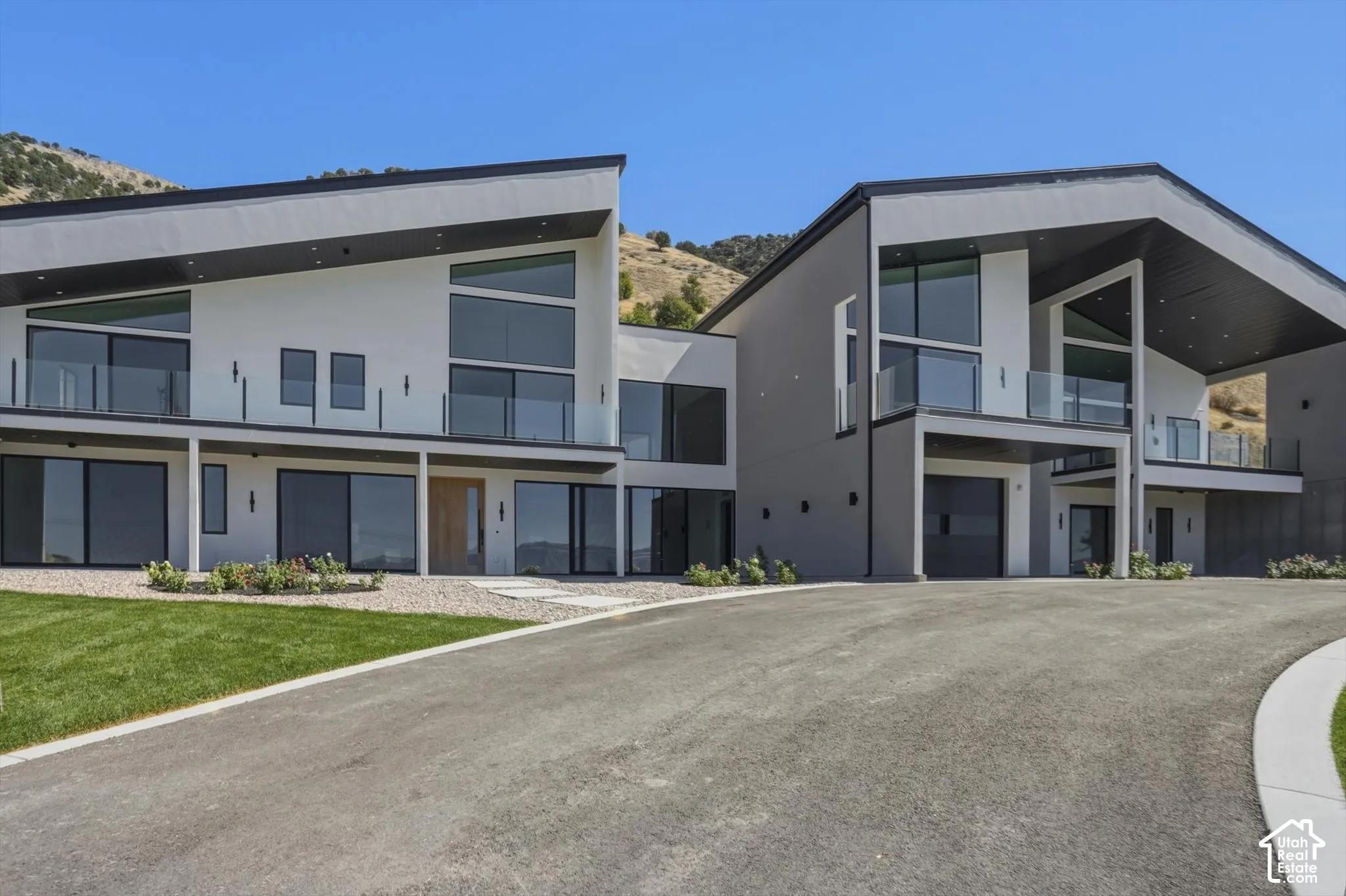 Modern architectural design featuring expansive glass panels, multiple glass-railed balconies, a covered entry, and an integrated garage