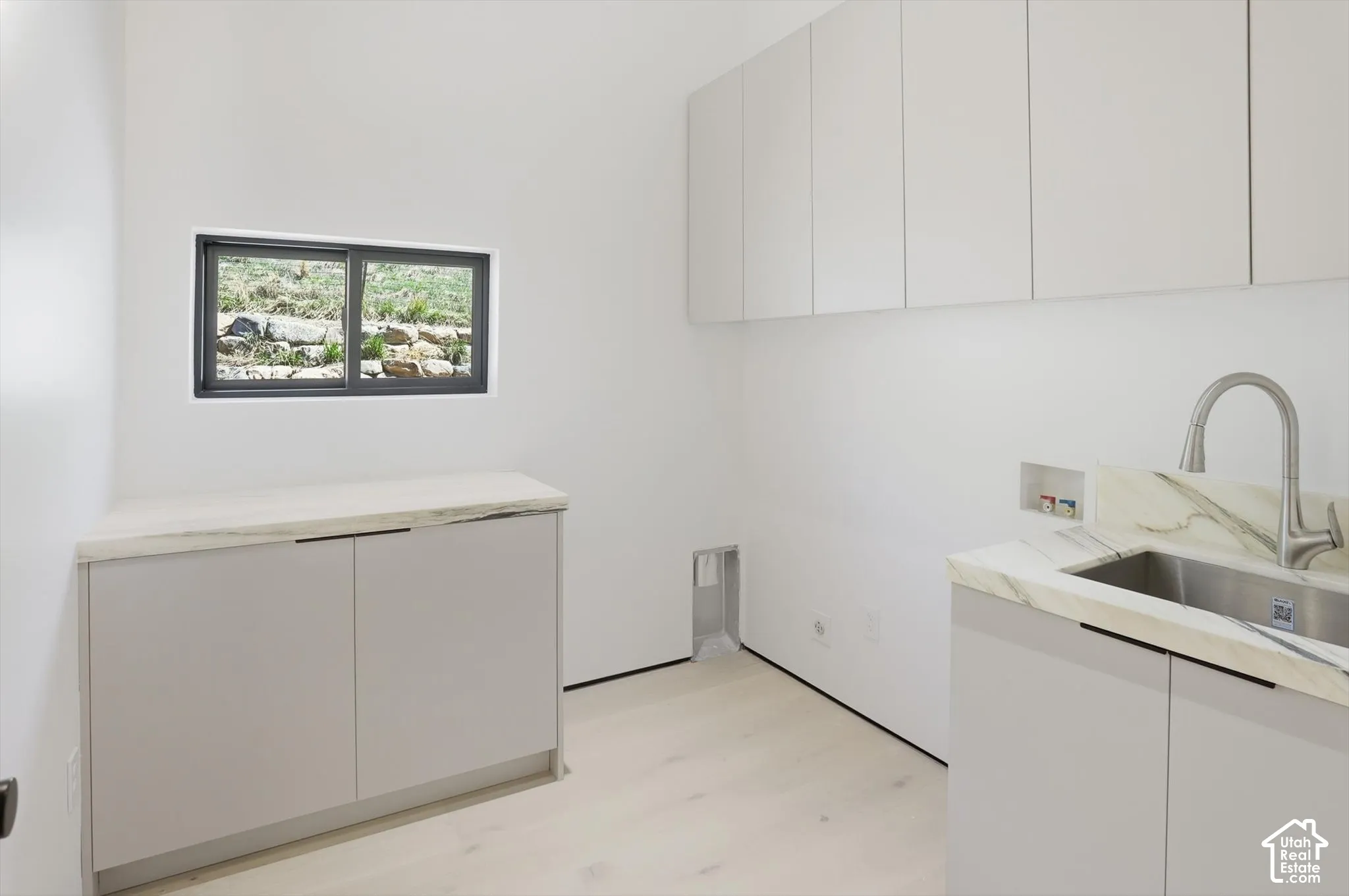 Light wood-finish flooring, white walls, built-in cabinetry, and a stainless steel sink with a gooseneck faucet