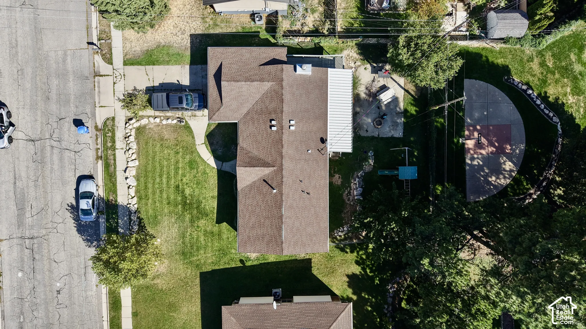 Expansive property featuring a paved driveway, front lawn, pitched roof, rear patio with cover, and a paved half-court