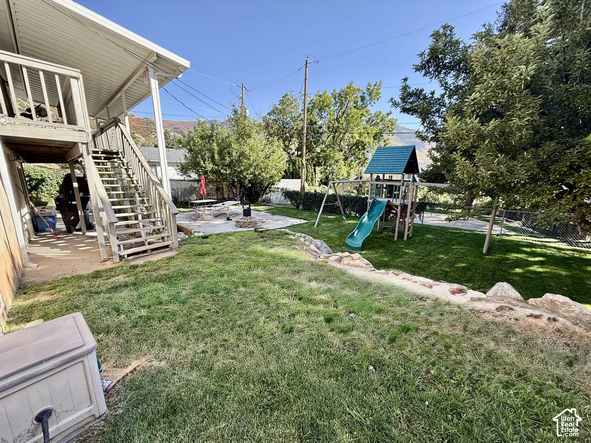 Expansive lawn area with a multi-level deck and stairs, featuring a paved patio with a fire pit