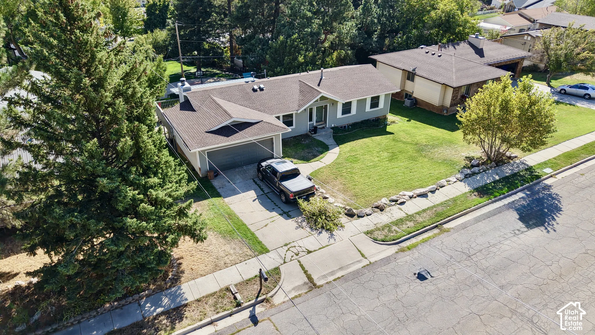 Pitched roofline, attached garage, concrete driveway, and front lawn with mature trees