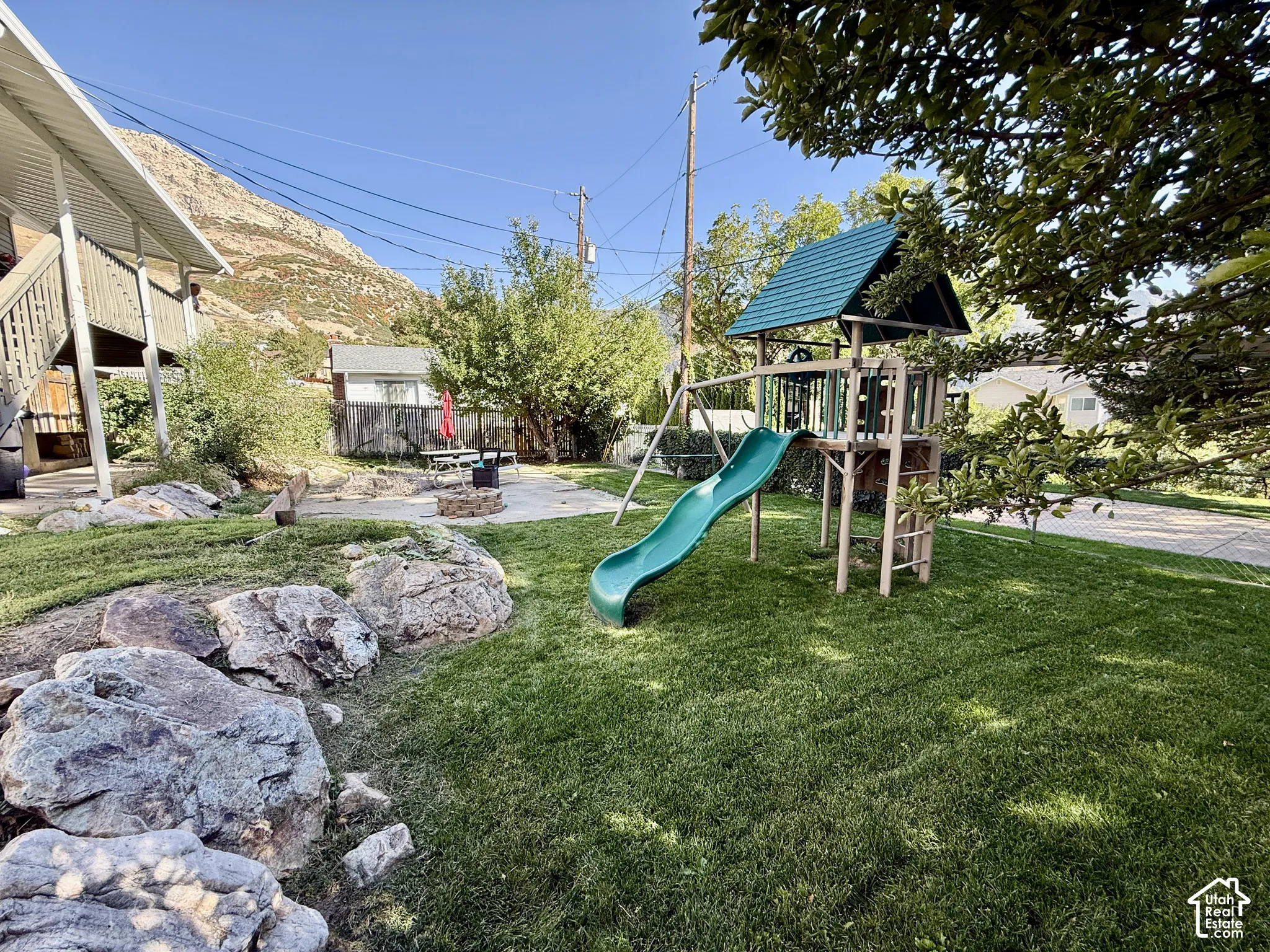 Expansive backyard featuring a manicured lawn, a play structure with slide, and a concrete patio area with a fire pit