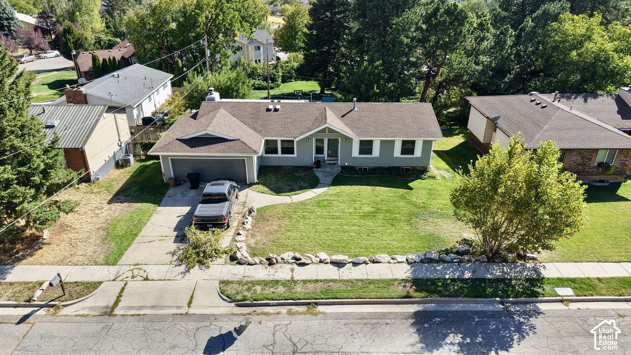 Single-story residence featuring a front yard, a driveway, a two-car garage, and mature trees