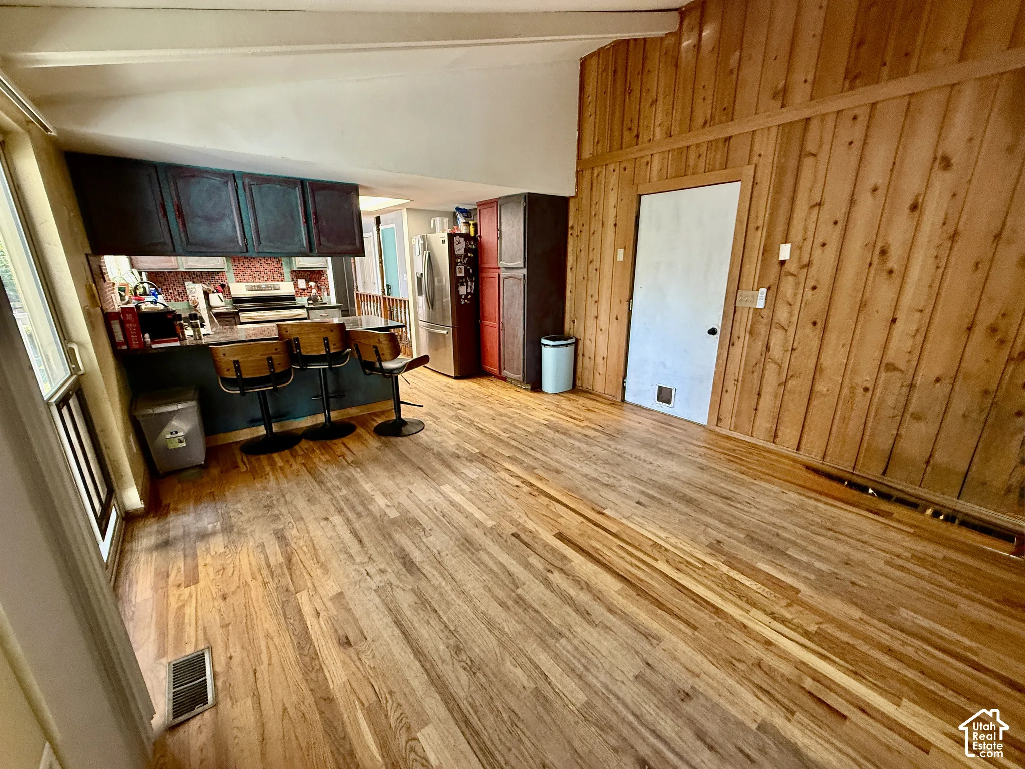 Hardwood flooring spans the open living area and kitchen, featuring a built-in breakfast bar with a solid surface countertop, wood paneling, and painted cabinetry