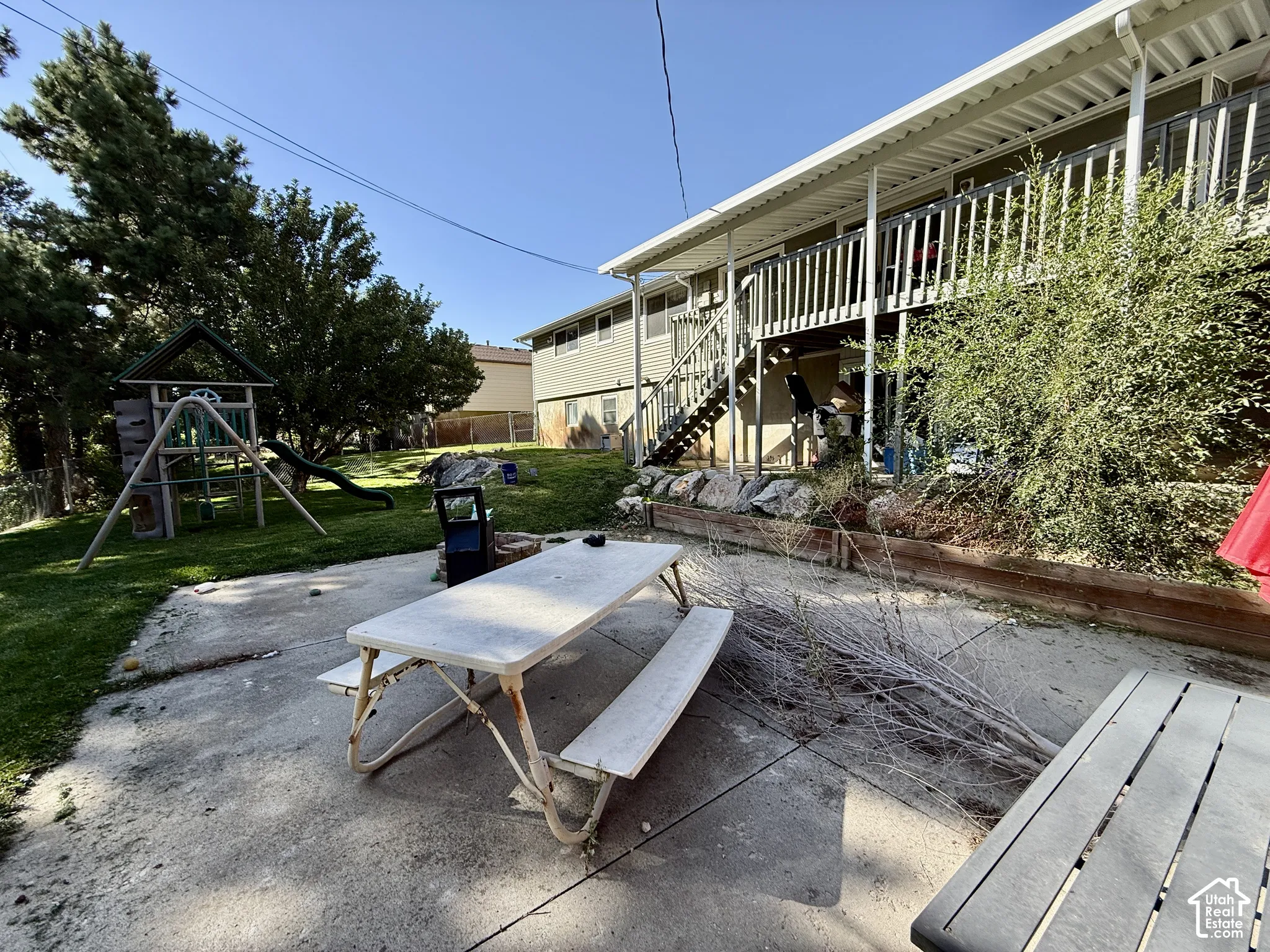 Expansive concrete patio with a detached outdoor play structure and a multi-level deck featuring railing