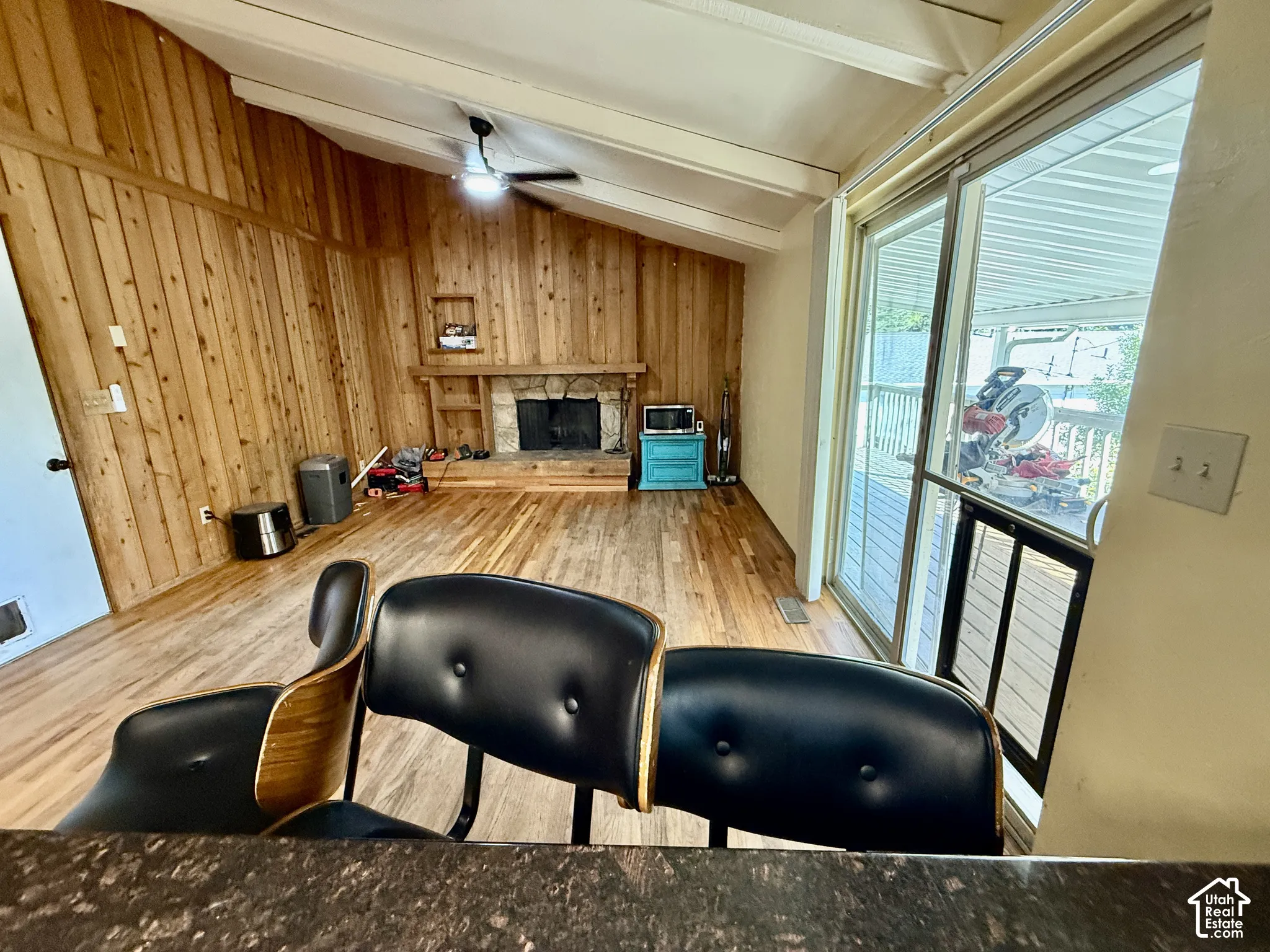 Vaulted wood-paneled ceiling, wood-finish flooring, stone-faced fireplace with hearth, and sliding glass door to exterior