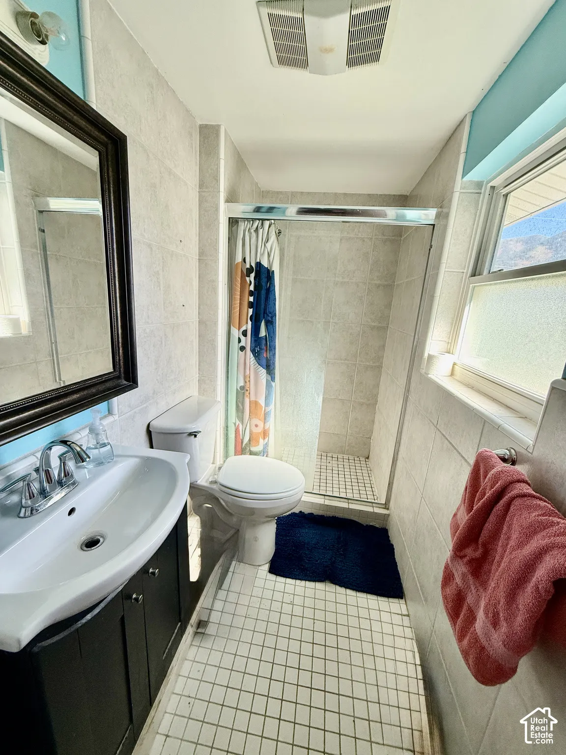 Vanity with integrated sink, framed mirror, tiled walls, tiled shower with glass enclosure, and tiled flooring
