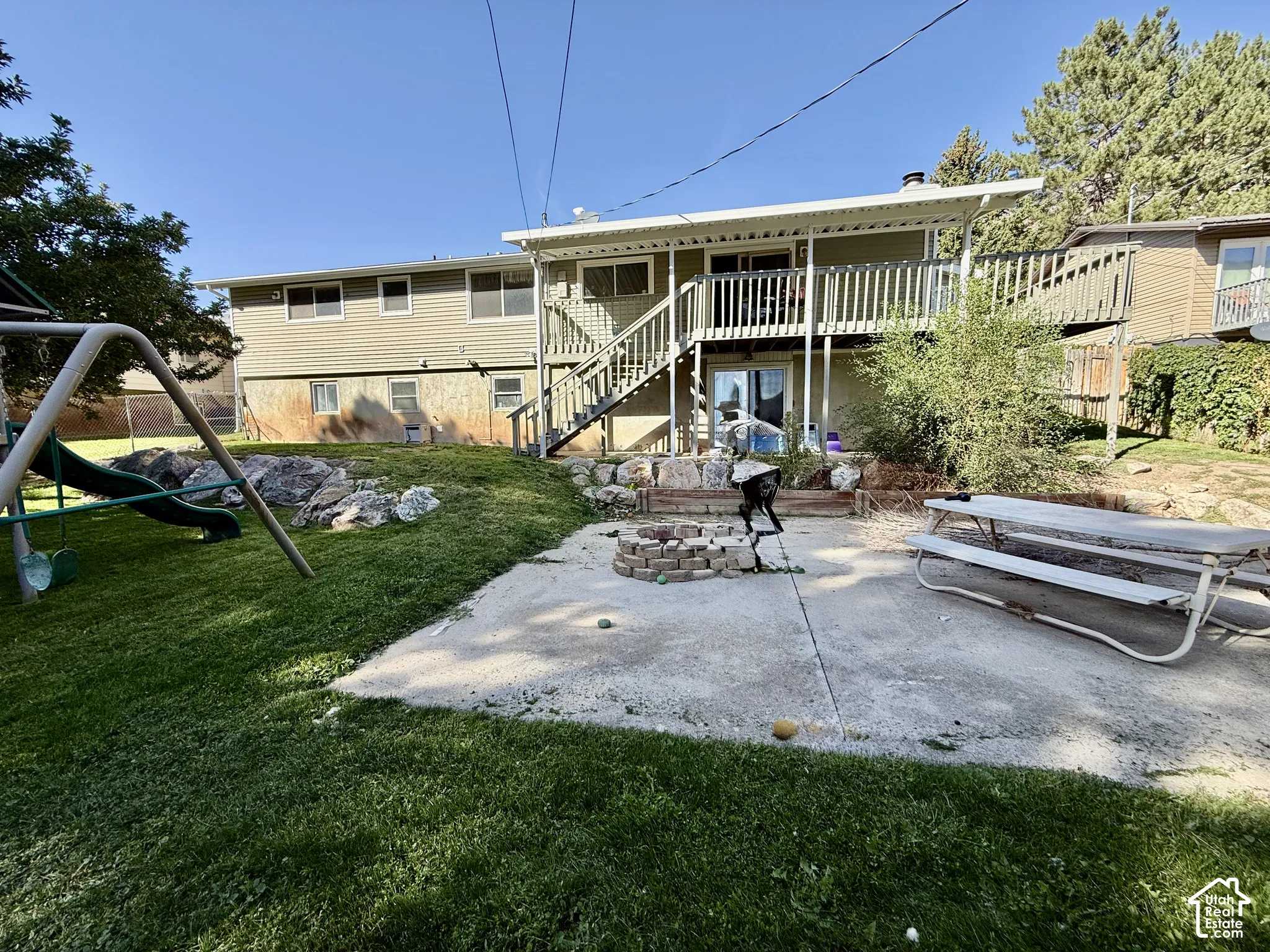 Expansive backyard featuring a concrete patio, a stone-lined fire pit, and a grassy area with mature trees