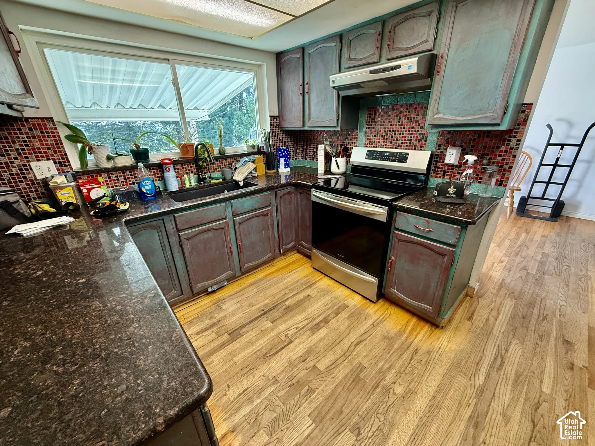 Kitchen featuring wood-finish flooring, dark speckled countertops, mosaic tile backsplash, a stainless steel range, and a window above the sink