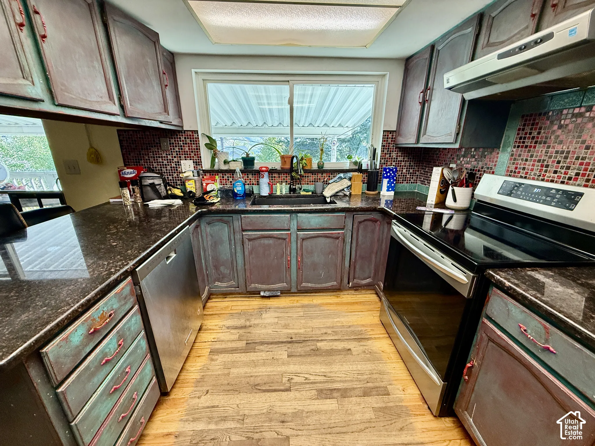 U-shaped kitchen featuring wood-finish flooring, dark speckled countertops, mosaic tile backsplash, and stainless steel appliances