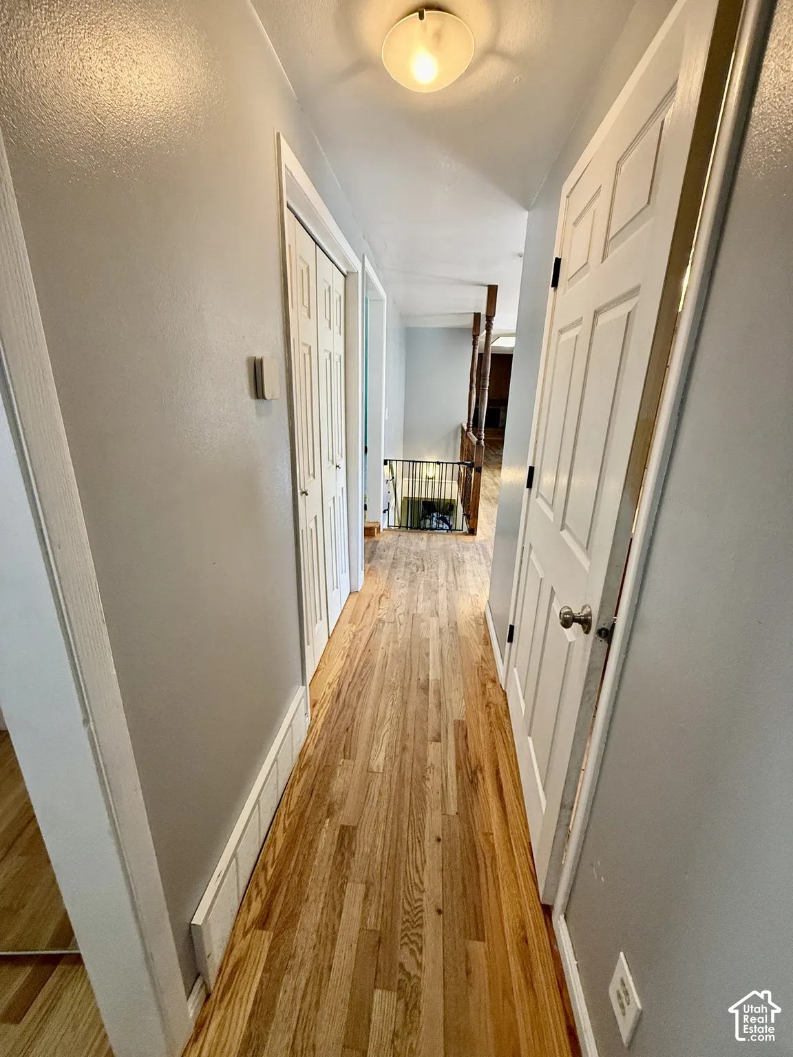 Hardwood flooring extends throughout this hallway, featuring a ceiling-mounted light fixture, white interior doors, and panel-style closet doors