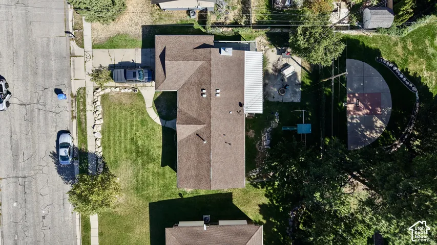 Expansive property featuring a paved driveway, front lawn, pitched roof, rear patio with cover, and a paved half-court