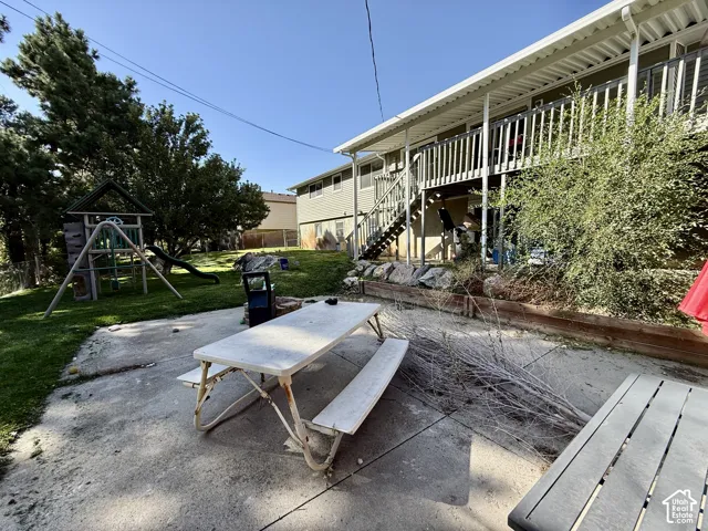 Expansive concrete patio with a detached outdoor play structure and a multi-level deck featuring railing