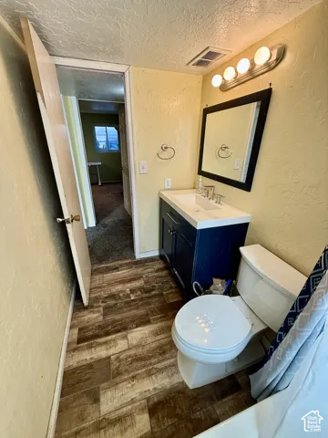 Wood-finish plank flooring, vanity with integrated sink, wall-mounted mirror, and four-bulb vanity lighting