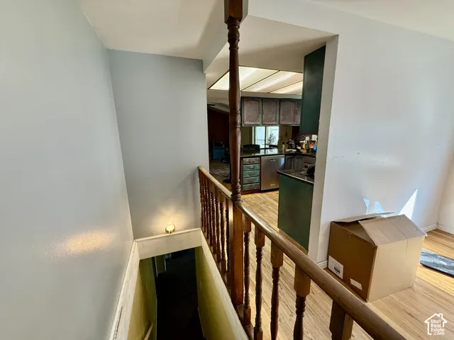 Wood-finish flooring, wooden baluster railing, recessed lighting, and a partial kitchen with cabinetry and stainless steel appliances