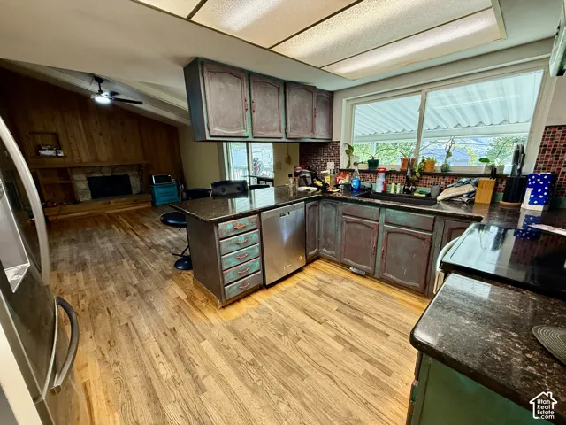 Hardwood flooring, kitchen island with built-in storage, stainless steel dishwasher, dark stone countertops, and a tiled backsplash