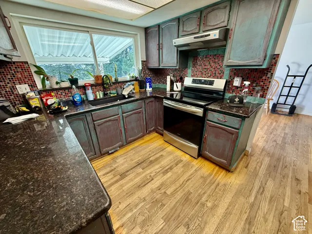 Kitchen featuring wood-finish flooring, dark speckled countertops, mosaic tile backsplash, a stainless steel range, and a window above the sink
