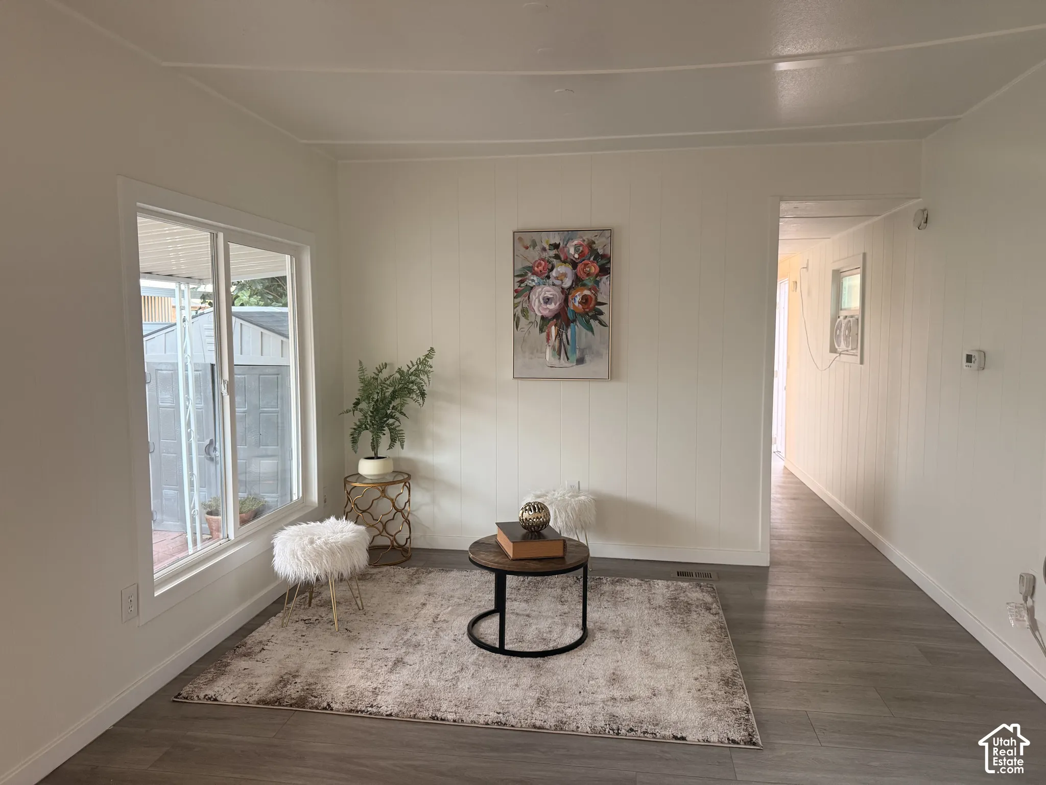 Light-filled interior space with wood-finish flooring, white vertical paneled walls, and a large sliding window