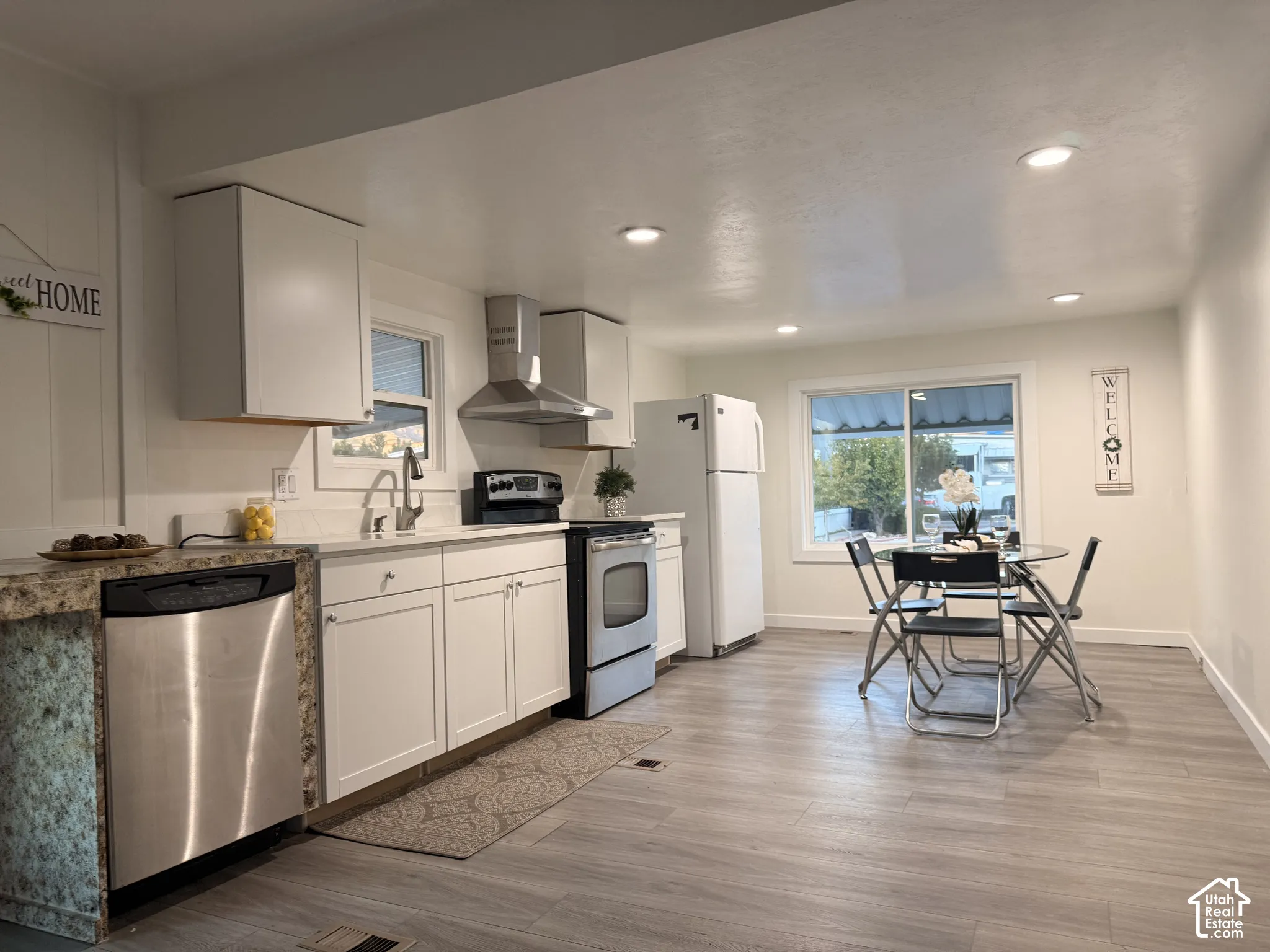 Kitchen featuring white cabinetry, stainless steel appliances, recessed lighting, and laminate flooring.
