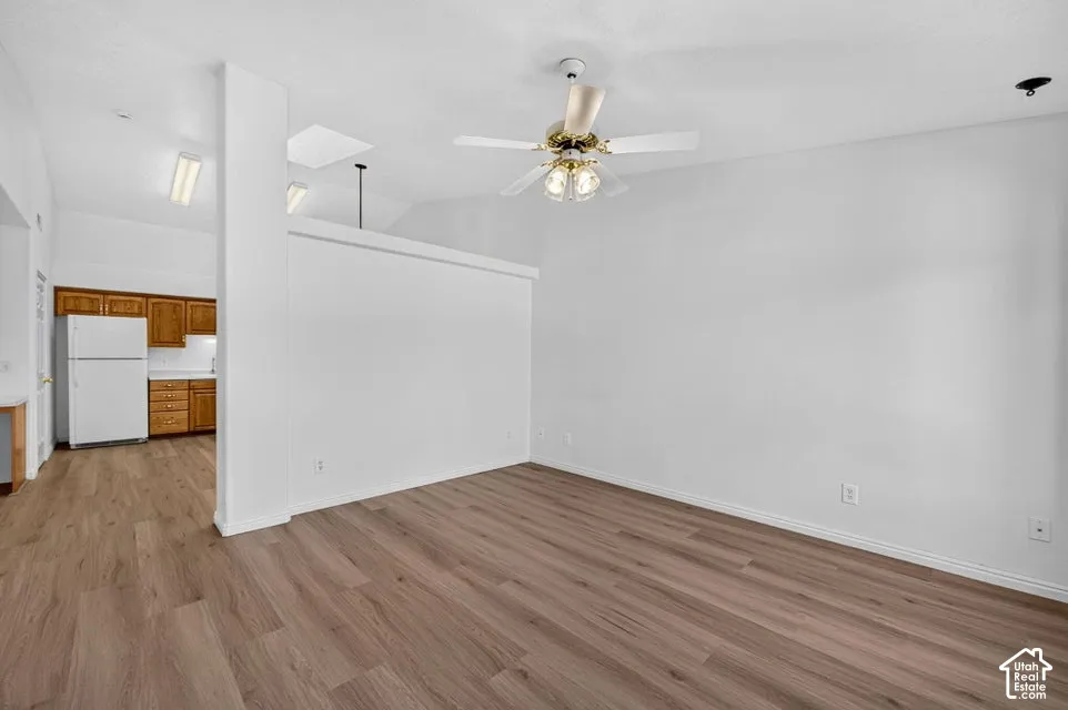 Wood-finish flooring throughout, white walls, and a ceiling fan with integrated lighting