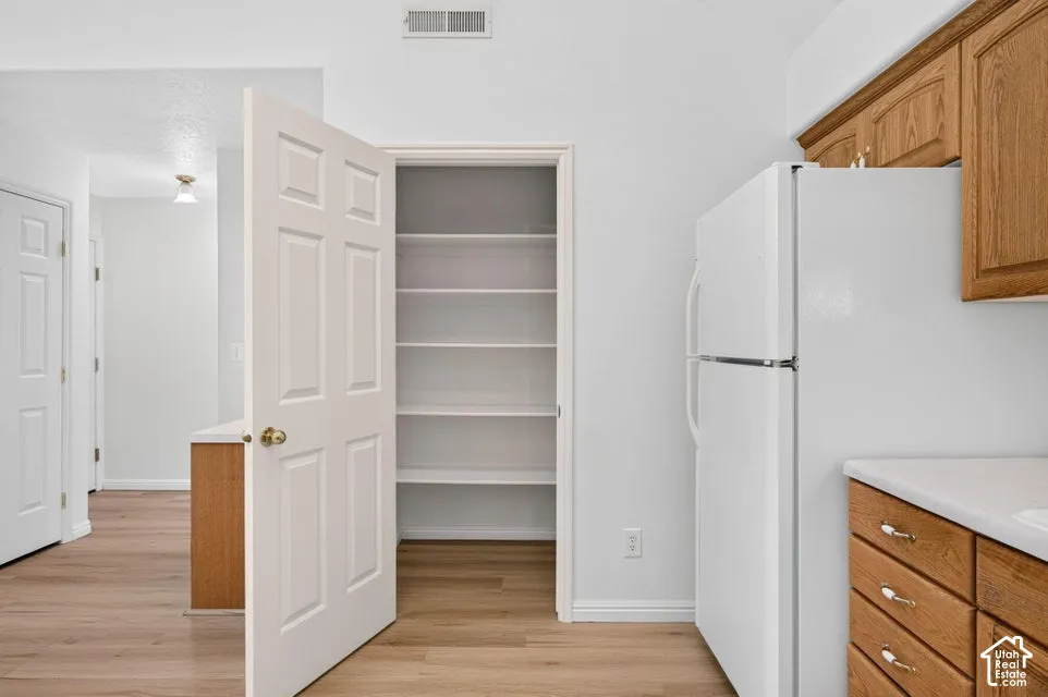 Kitchen featuring wood-finish flooring, wood cabinetry with decorative pulls, white countertop, and a built-in pantry with shelving