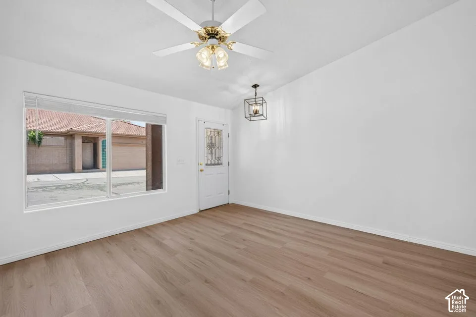 Wood-finish flooring, white walls, ceiling fan with integrated lighting, recessed window, and a decorative entry door with leaded glass