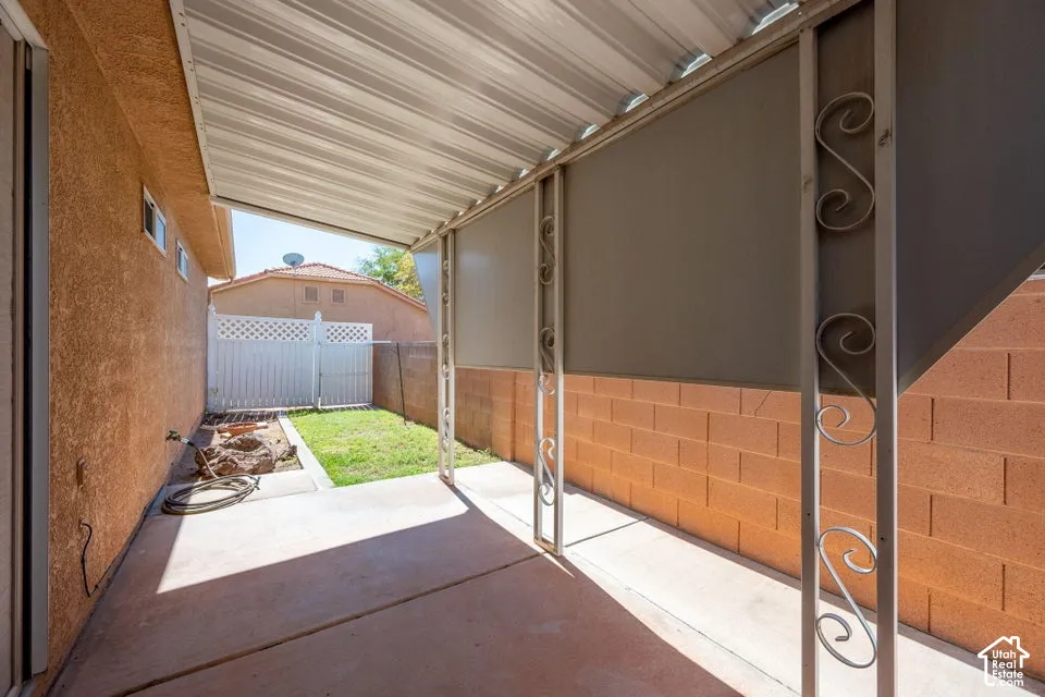 Covered patio with concrete flooring, stucco exterior wall, and decorative metal support columns
