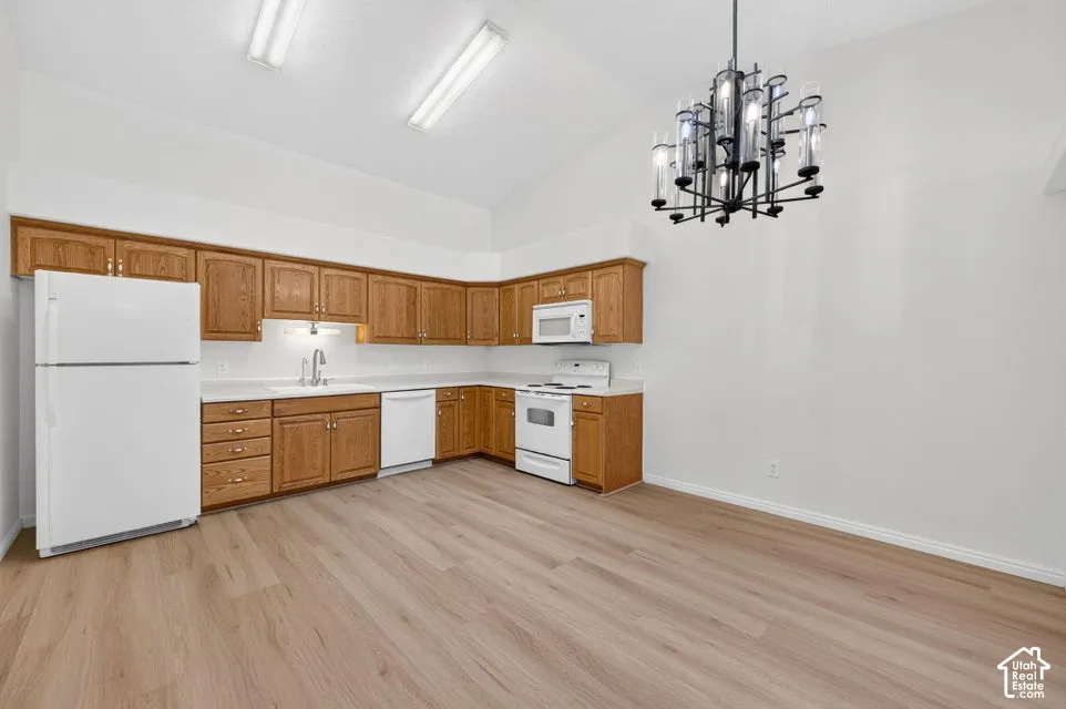 Kitchen featuring wood-finish cabinetry, white appliances, light-toned countertops, vaulted ceiling, and wood-finish flooring