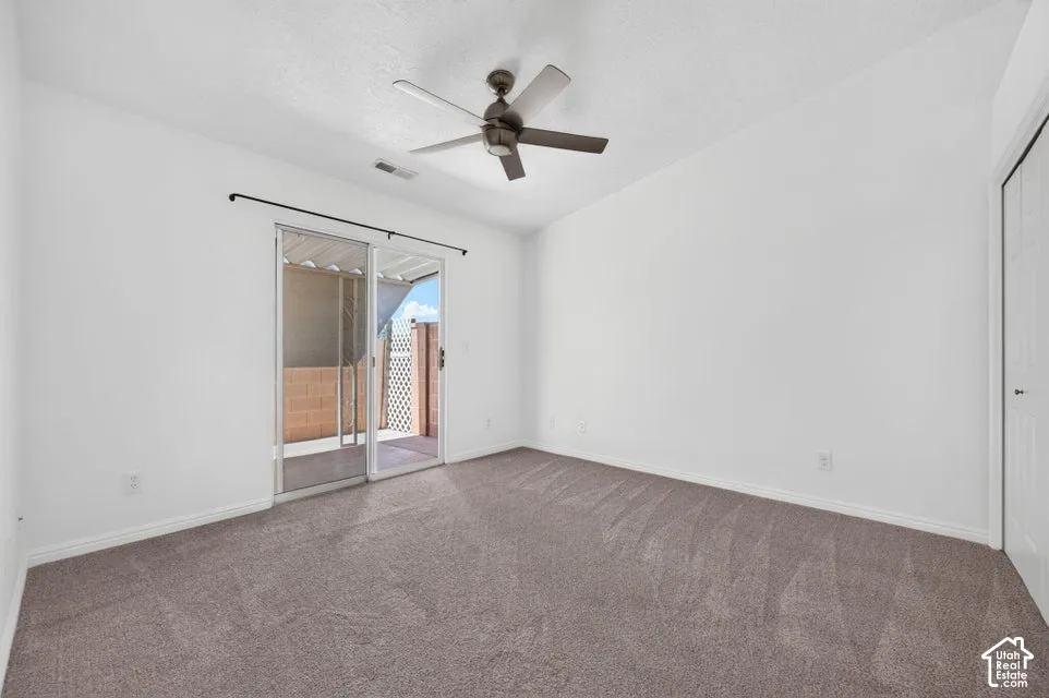 Neutral-toned carpet flooring, sliding glass door, overhead ceiling fan, and white walls