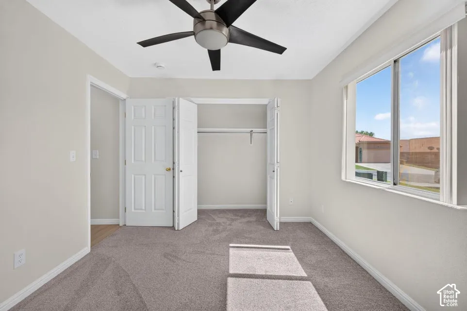 Carpeted flooring, bi-fold closet doors, ceiling fan with light, and a large window