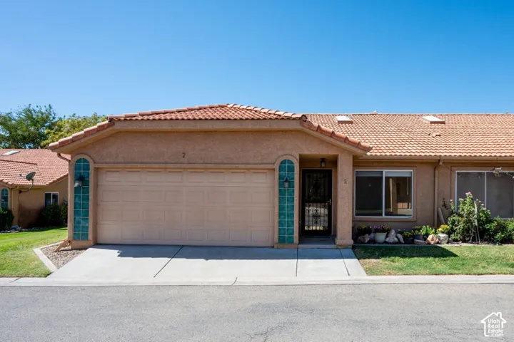 Stucco exterior with a terracotta tile roof, attached garage, concrete driveway, and front entryway with decorative glass block accents