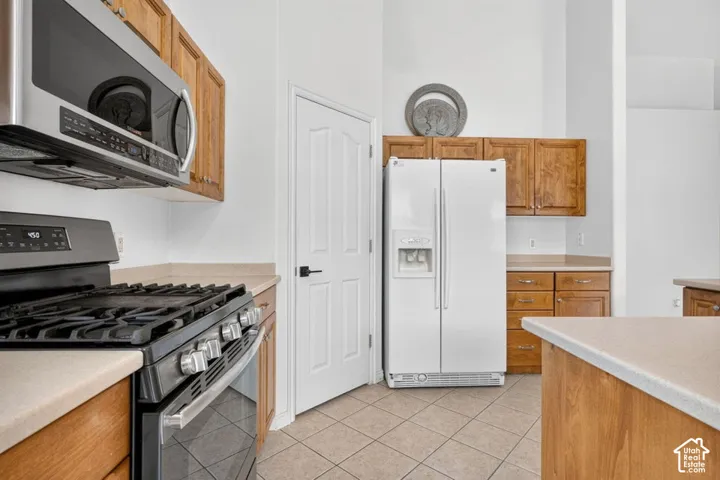 Kitchen featuring a stainless steel microwave and range, light wood cabinetry, light-toned countertops, and tiled flooring